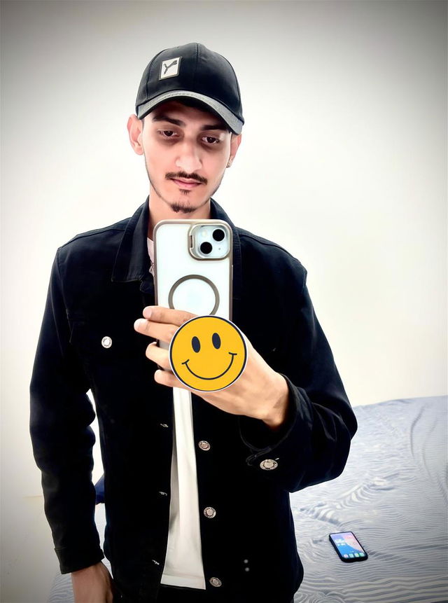 A stylish young man taking a mirror selfie, wearing a black denim jacket over a white t-shirt