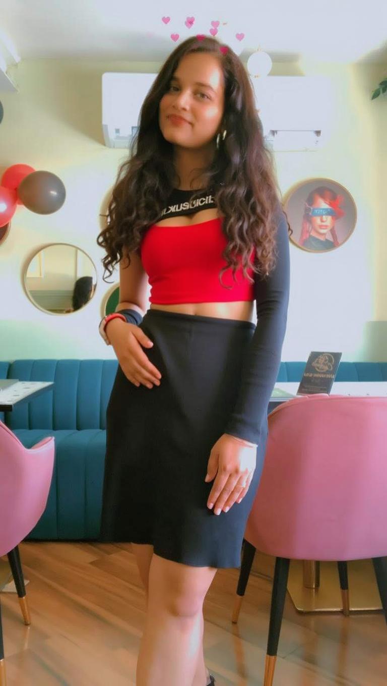 A confident woman standing in a stylish café, wearing a fashionable red crop top paired with high-waisted jeans