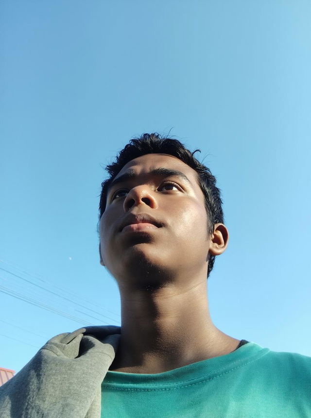 A young person with a tapper fade hairstyle, standing against a clear blue sky