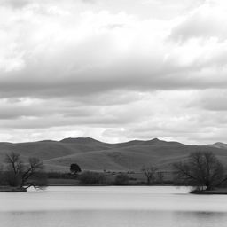 A high resolution, black and white image of a serene landscape featuring rolling hills under a cloudy sky
