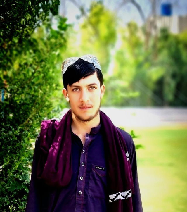 A young man standing confidently in a serene outdoor setting, surrounded by lush green foliage