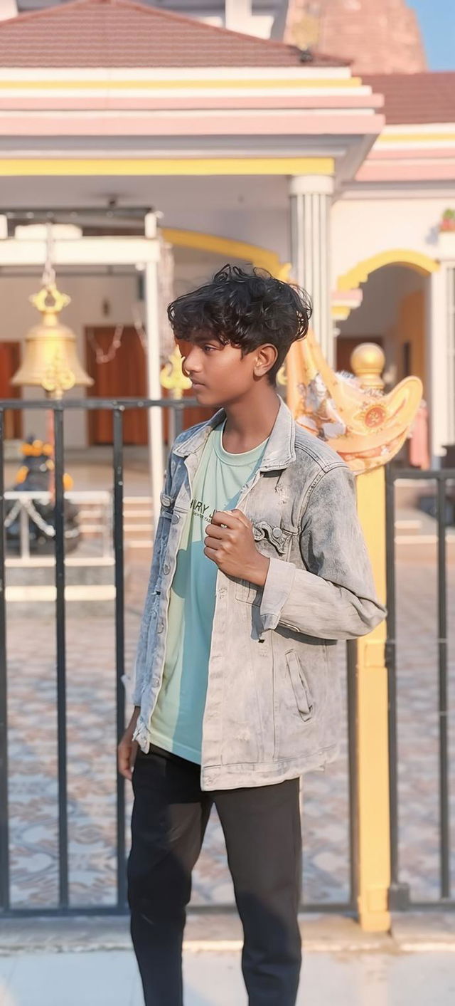 A teenage boy standing confidently outside a vibrant temple, wearing a stylish outfit