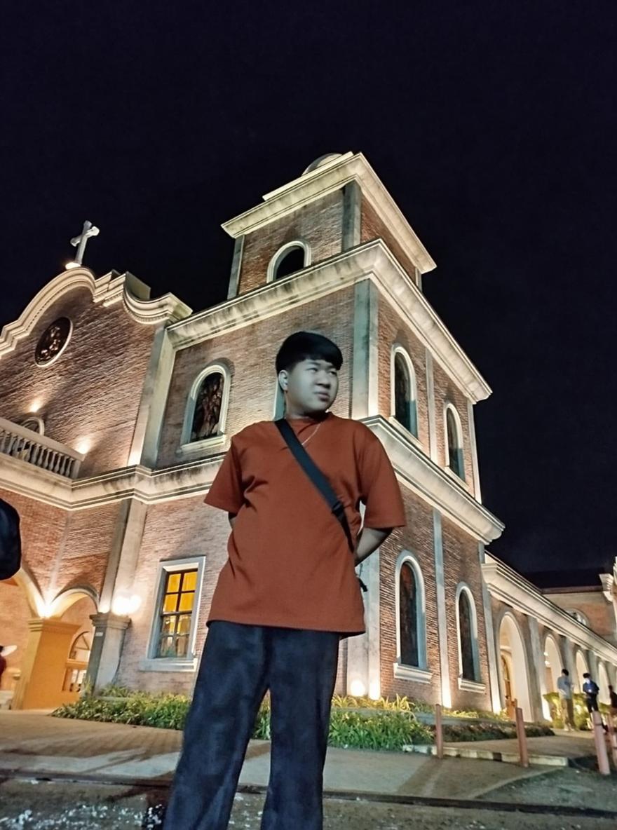 A young man standing in front of a beautifully lit brick church at night