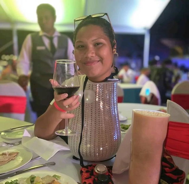 A cheerful woman sitting at a beautifully set table, smiling and holding a glass of red wine