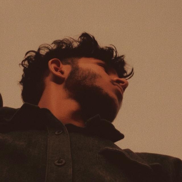 A close-up portrait of a young man with a confident expression, showcasing his stylish hairstyle and facial hair