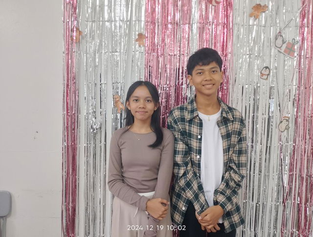 A joyful scene featuring two teenagers hugging warmly in front of a festive backdrop adorned with shiny silver and pink tinsel