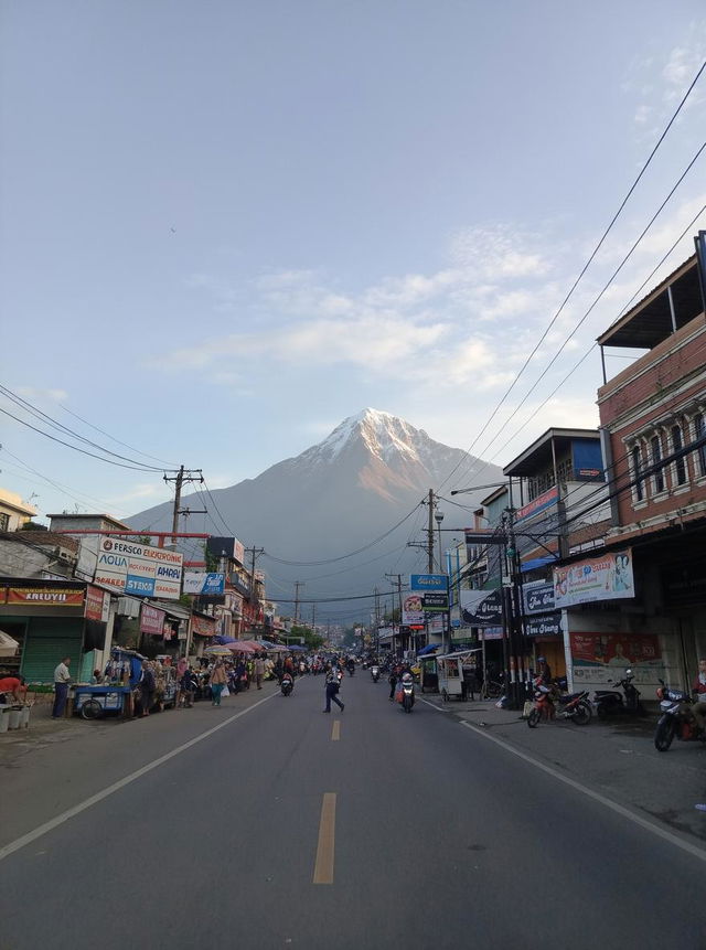 A busy street scene in a small town with shops and vendors, surrounded by mountains in the background