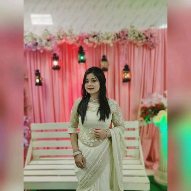 A woman wearing a traditional saree, elegantly posed in a beautifully decorated indoor setting