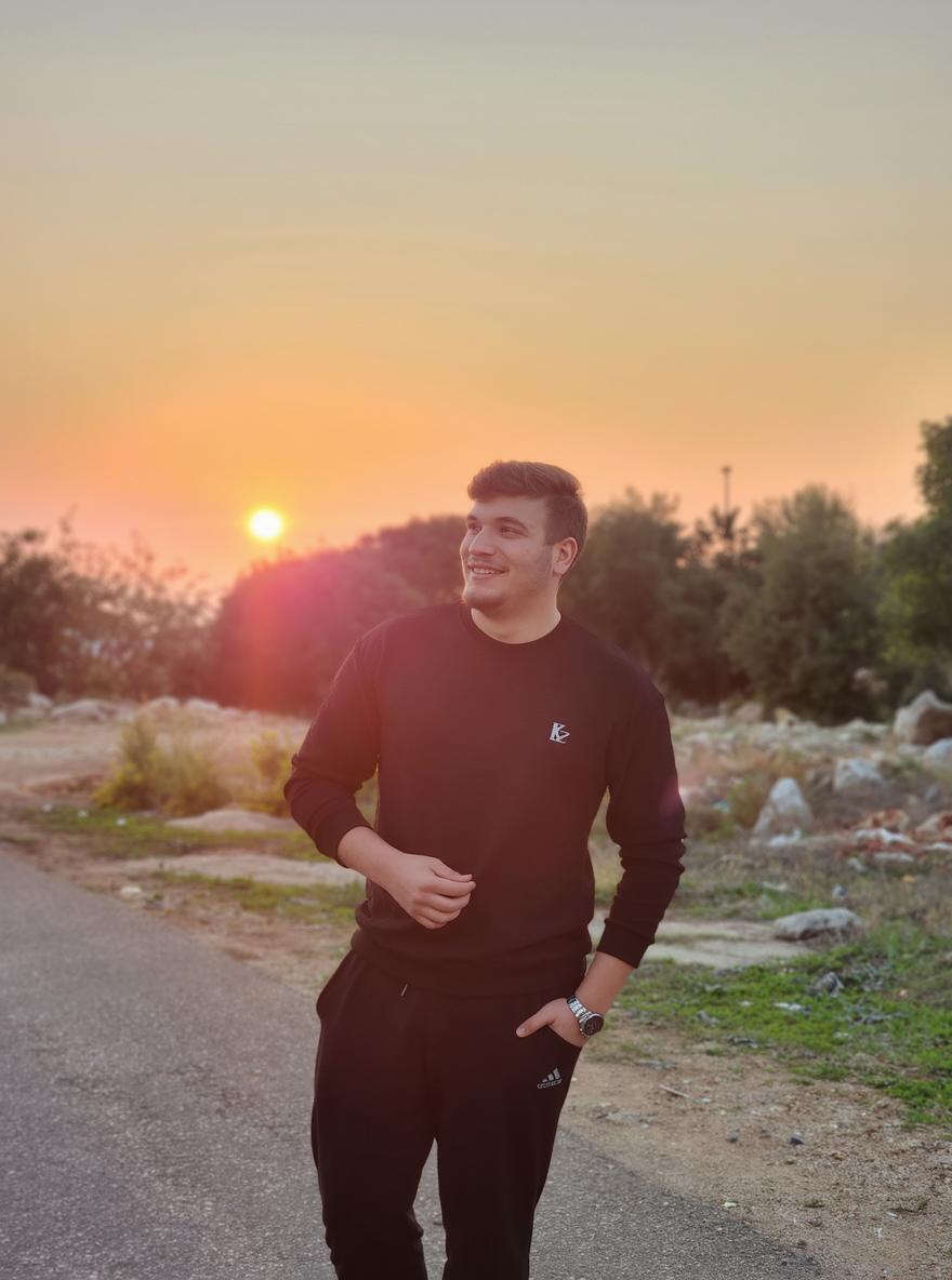 A young man standing confidently on a winding road at sunset, dressed in a formal suit