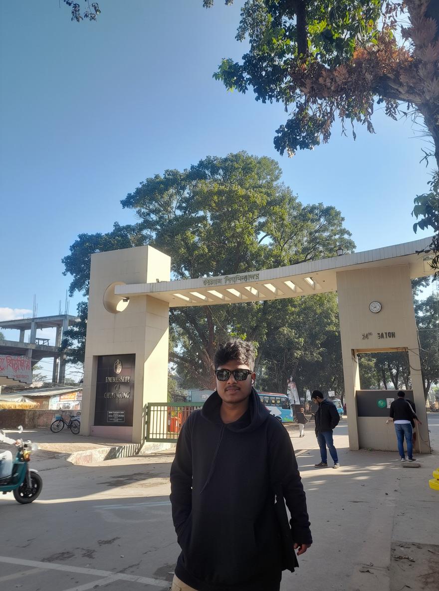 A bright, sunny day captured at an entrance gate of a university, featuring a young man with a glowing and vibrant expression