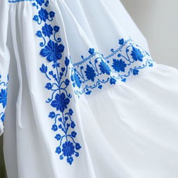 A beautiful white garment with intricate blue embroidery, showcasing delicate floral and geometric patterns
