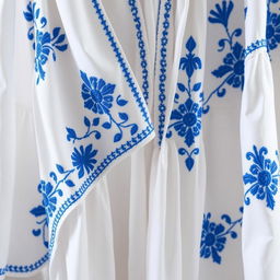 A beautiful white garment with intricate blue embroidery, showcasing delicate floral and geometric patterns