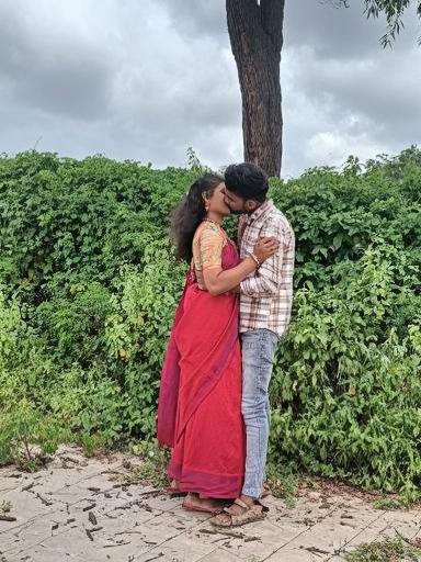 A romantic couple sharing a kiss in an outdoor setting, surrounded by lush green foliage