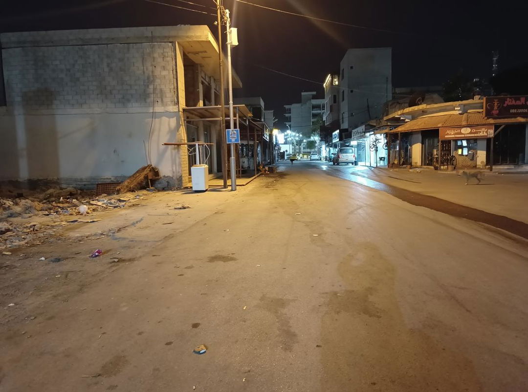 A serene nighttime street scene in a small town, showcasing an empty road illuminated by soft streetlights