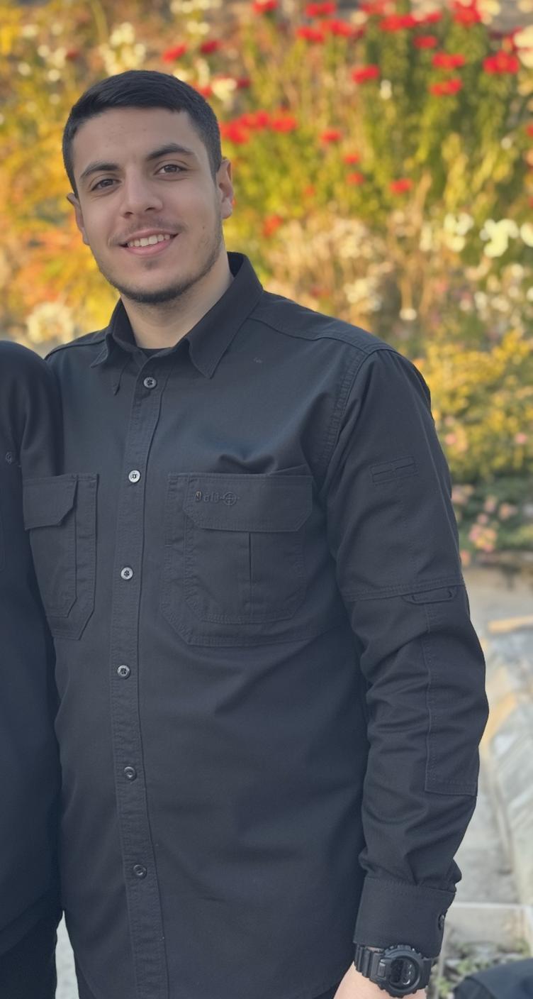 A 40-year-old man standing outdoors, wearing a black button-up shirt