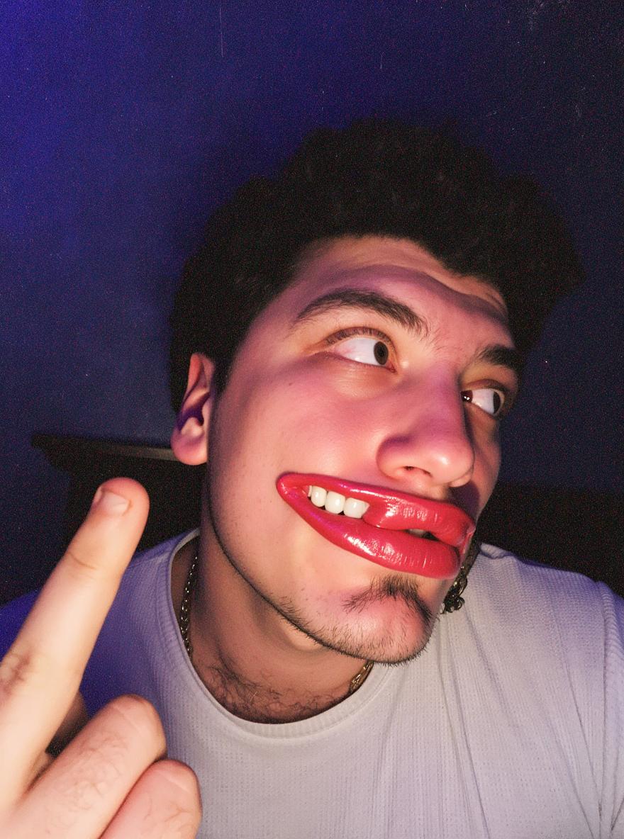 A young man playfully posing with a cheeky expression, showcasing exaggerated lip gloss, dressed in a casual white shirt