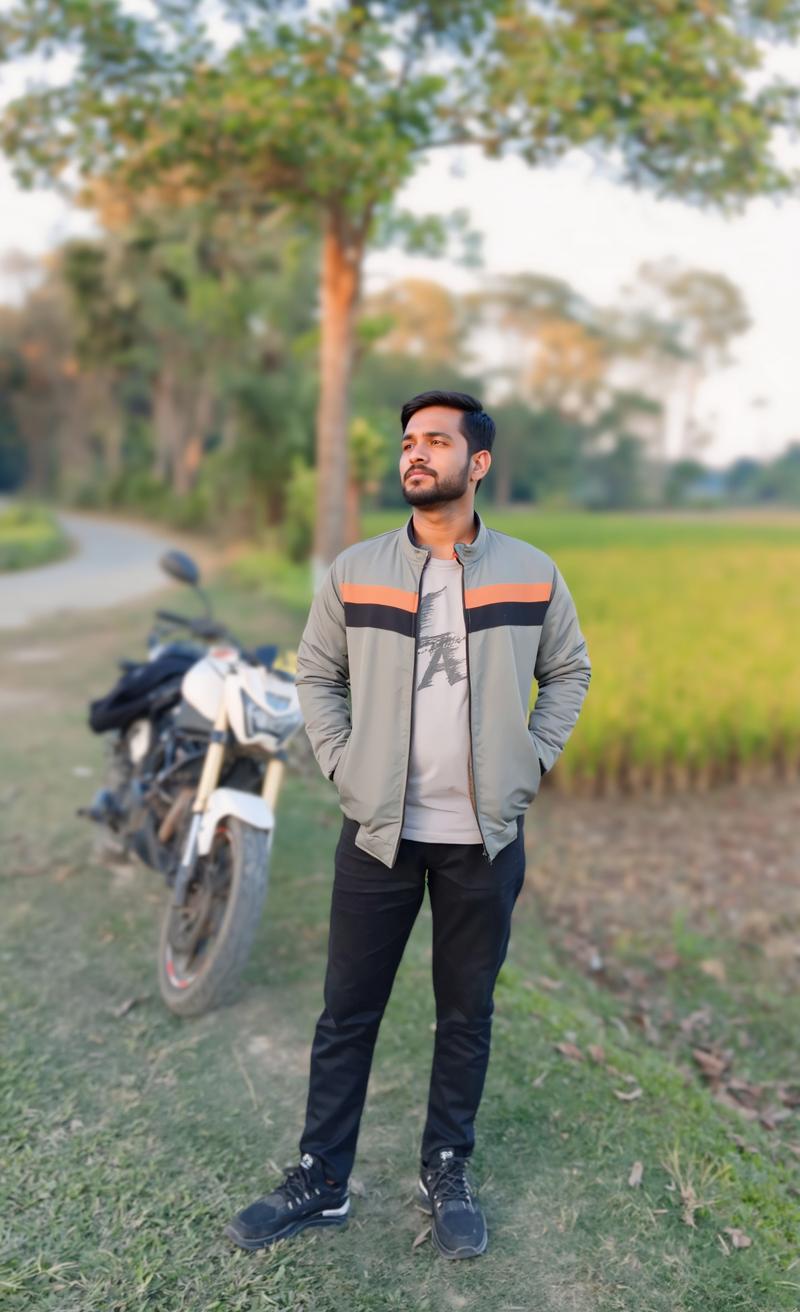 A stylish young man standing confidently beside a motorcycle in a picturesque countryside setting