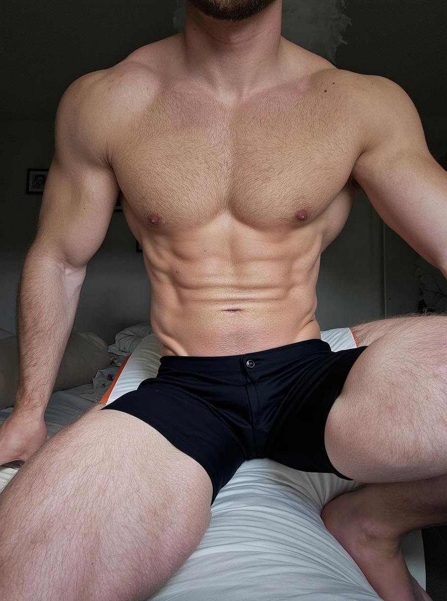 A muscular man sitting on a bed, wearing black shorts, showcasing an athletic build with defined abs and toned arms