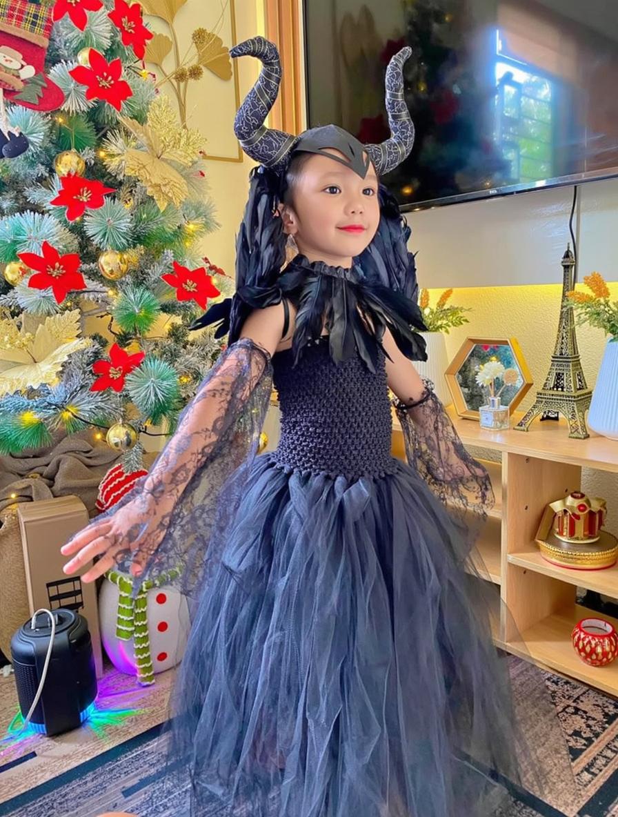 A young child dressed in an elaborate black costume resembling a forest fairy or dark queen, complete with feathered accents, a lace bodice, and a tulle skirt