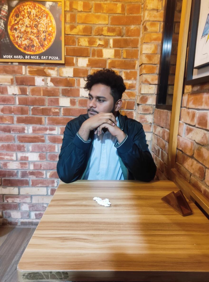 A young man sitting pensively at a wooden table in a cozy restaurant