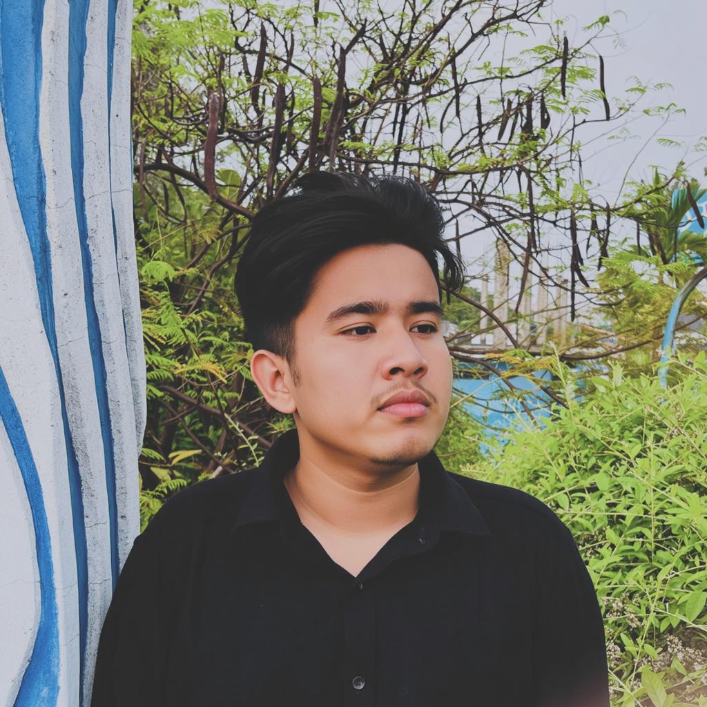 A young man with a sharp jawline, standing thoughtfully against a vibrant background featuring lush greenery and a partially painted wall