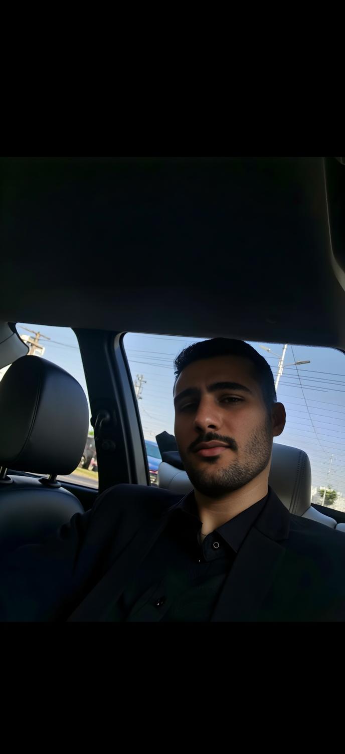 A young male seated in a car, wearing a formal outfit