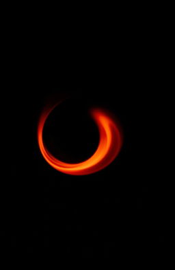 A small, captivating red flame swirling gracefully in a spiral against a completely black background