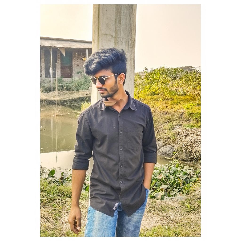 A young man wearing sunglasses, standing in a serene outdoor setting with a natural landscape