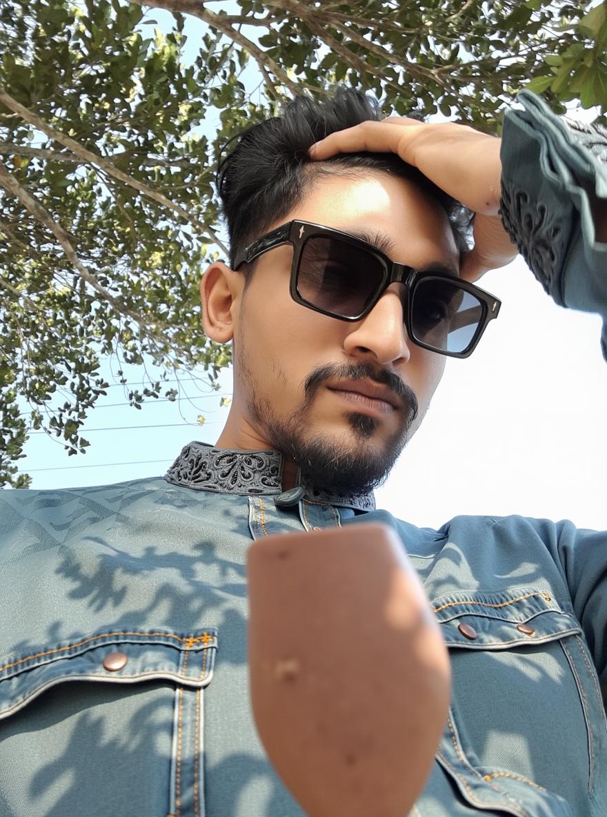 A stylish young man outdoors wearing a traditional patterned tunic with a modern twist, looking confidently at the camera while adjusting his sunglasses
