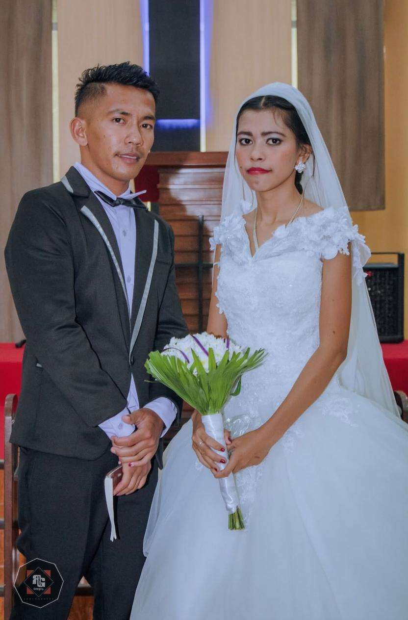 A beautifully decorated wedding scene, capturing a bride in a stunning white gown with lace details and a veil, standing beside her groom in a sharp black tuxedo