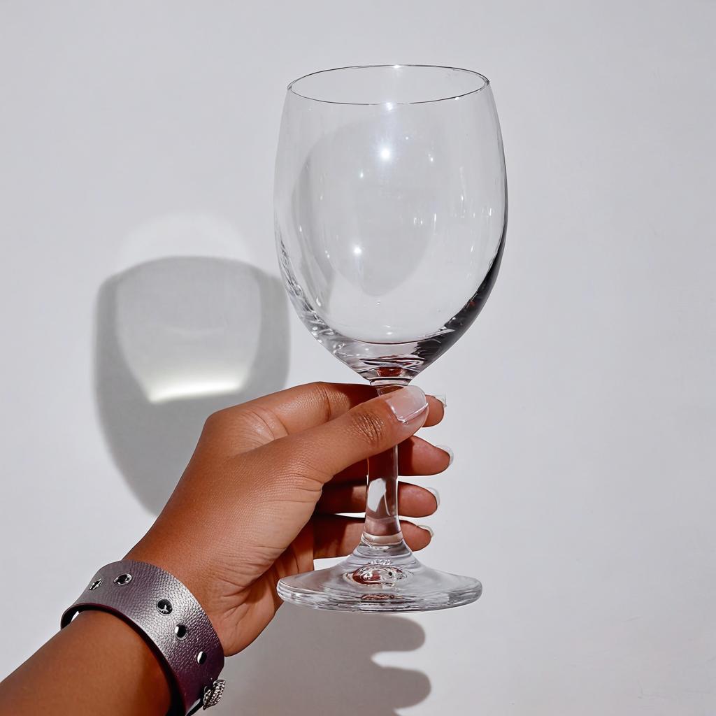 La mano izquierda de una mujer, agarrando una copa de vino tinto, y de fondo las