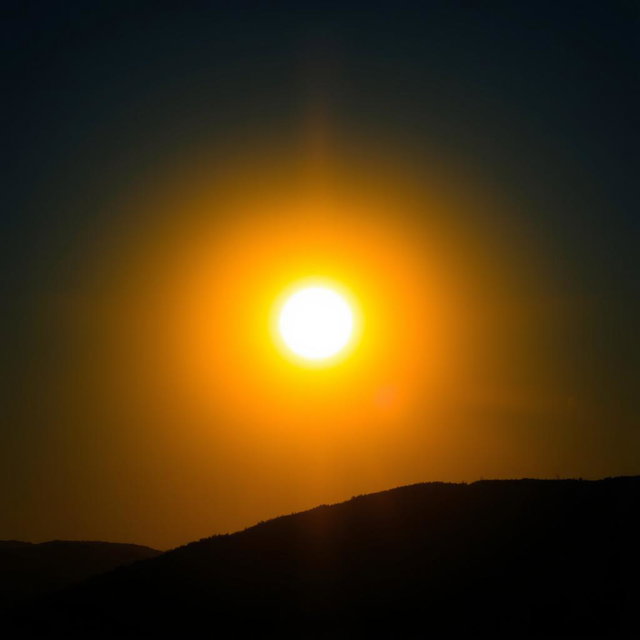 A vivid scene featuring a radiant sun shining brightly in a clear blue sky, illuminating the landscape with intense yellow and gold hues
