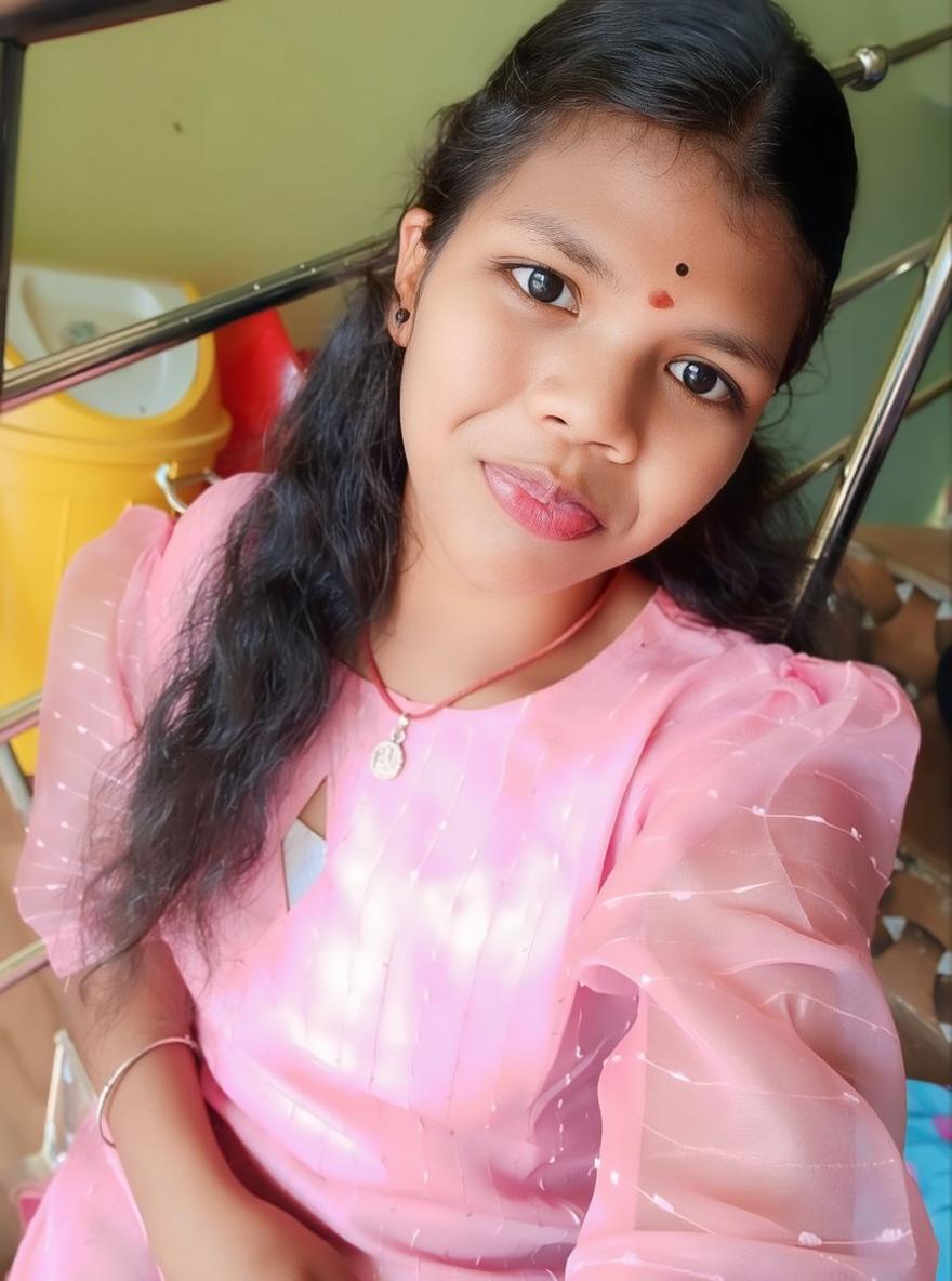 A young woman sitting casually, wearing a beautiful pink dress with puffed sleeves, smiling softly at the camera