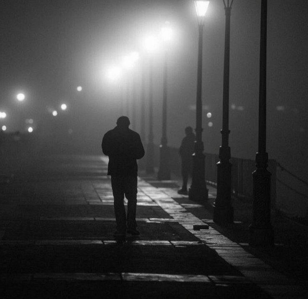 A couple walking down a foggy, atmospheric alleyway at night