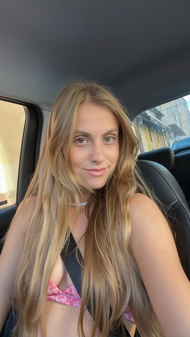 A young woman with long, flowing hair sitting in the driver's seat of a car, smiling gently at the camera