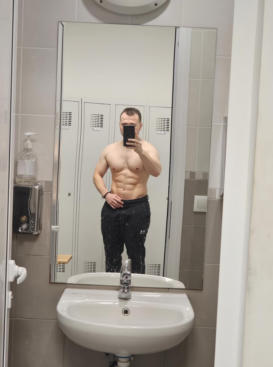 A fit and athletic male figure posing in front of a bathroom mirror