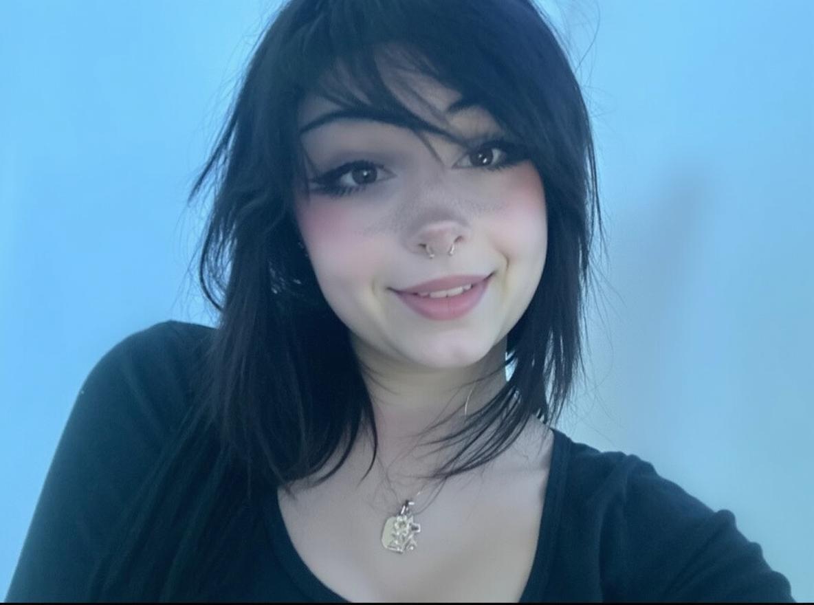 A portrait of a smiling young woman with long, black hair that has a playful coyness, set against a soft blue background