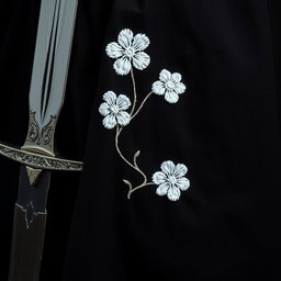 A close-up view of the folds of a small section of a black cloak, prominently displaying rough white flower embroidery