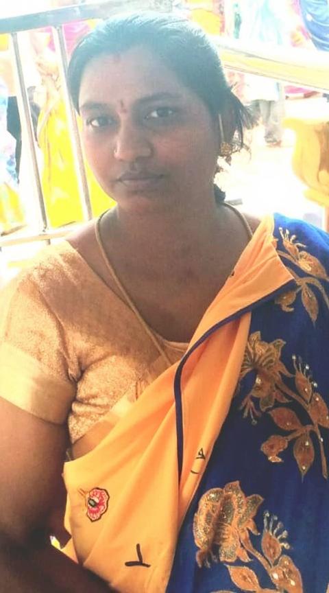 A woman sitting gracefully in traditional Indian attire, wearing a vibrant blue and orange saree adorned with intricate floral embroidery