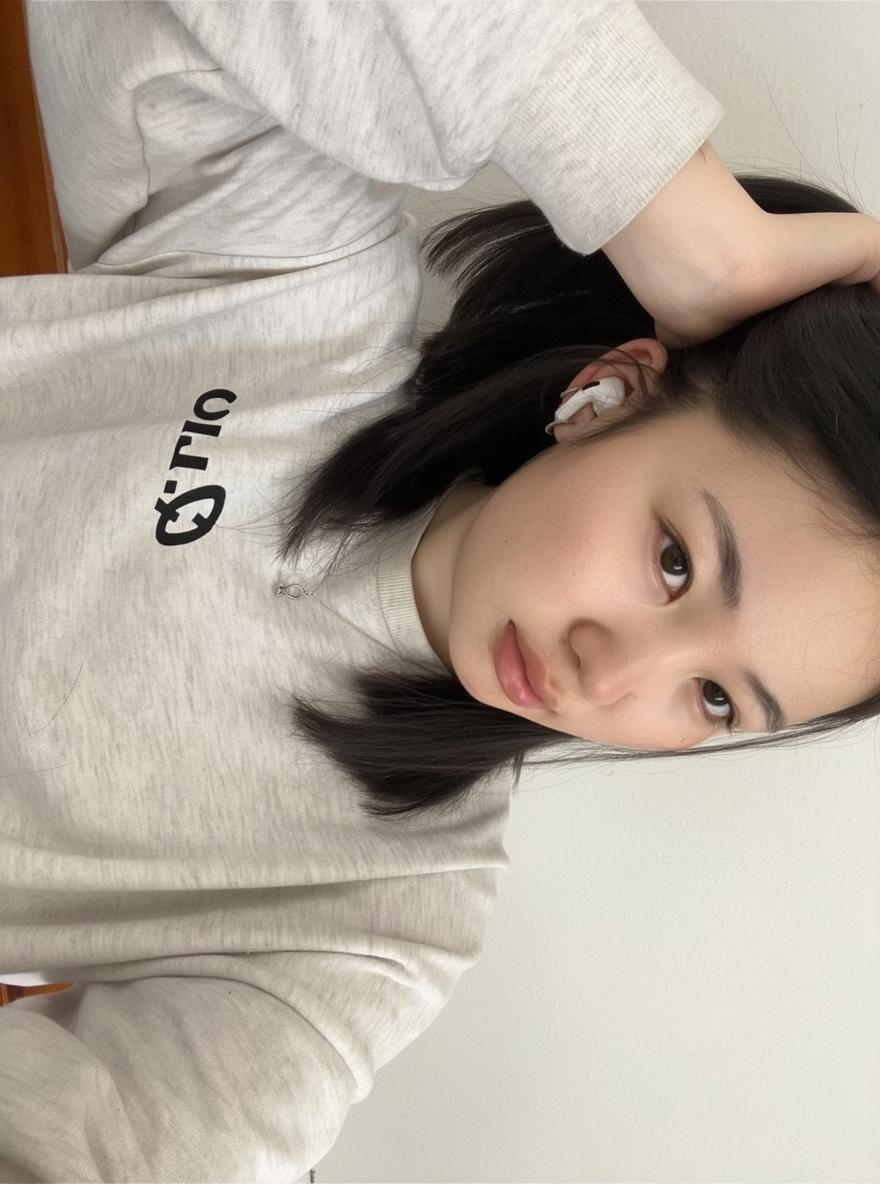 A casual young adult with straight black hair, wearing a light gray sweatshirt