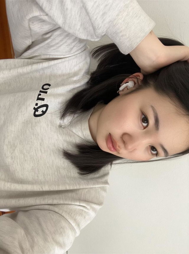 A casual young adult with straight black hair, wearing a light gray sweatshirt