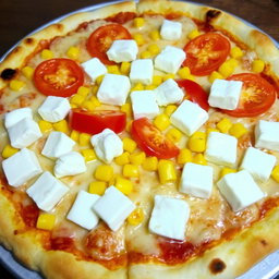 A delicious pizza featuring sweet corn and juicy tomatoes, generously topped with creamy paneer cubes