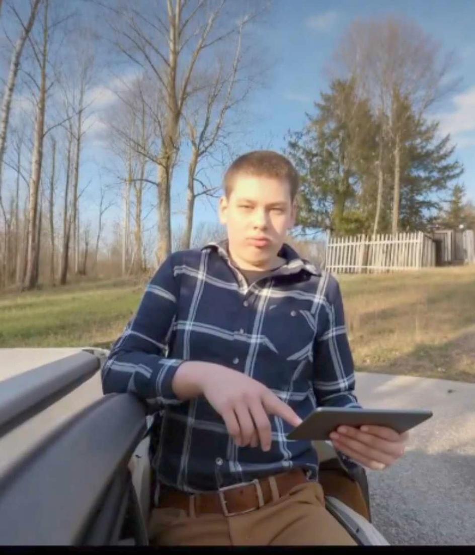 A young person sitting on the edge of a car, reading a book instead of a tablet