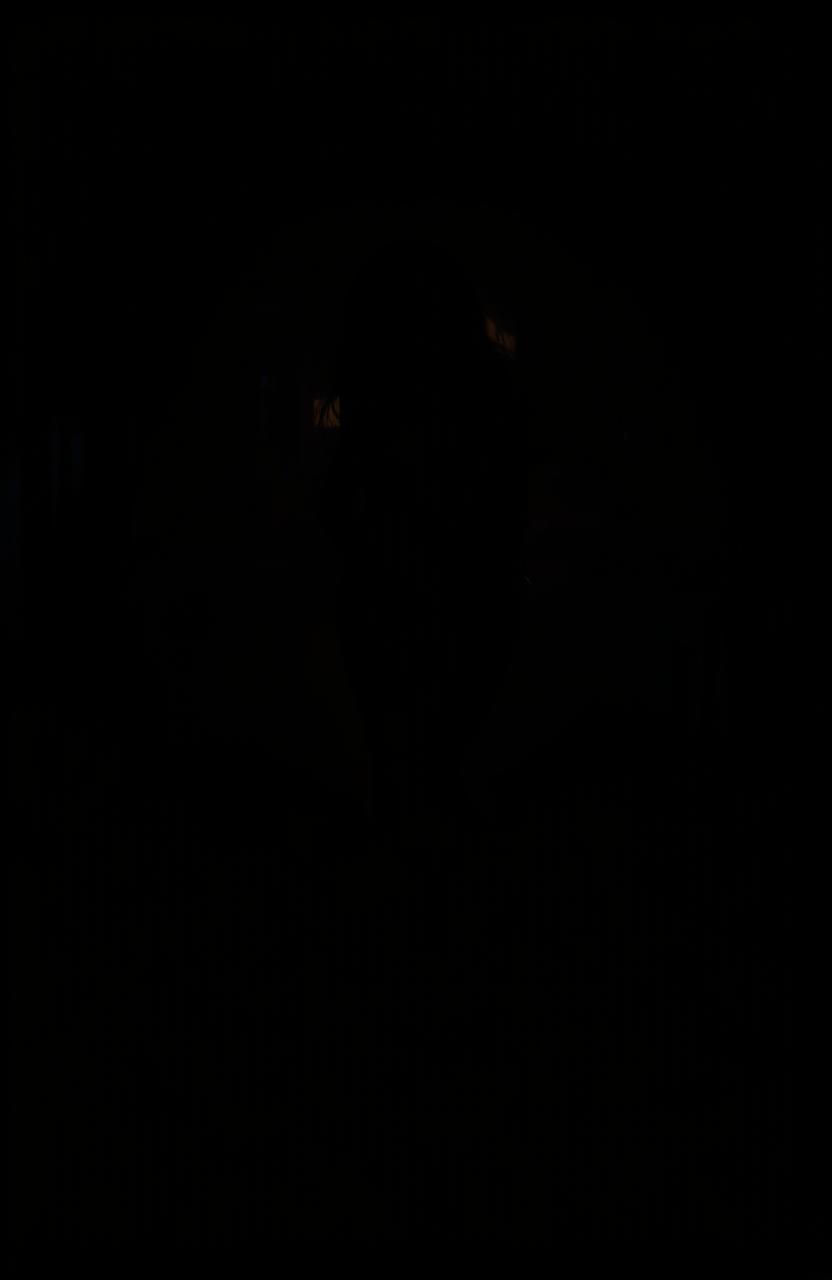 A mysterious scene set in darkness, featuring the silhouette of a woman standing gracefully