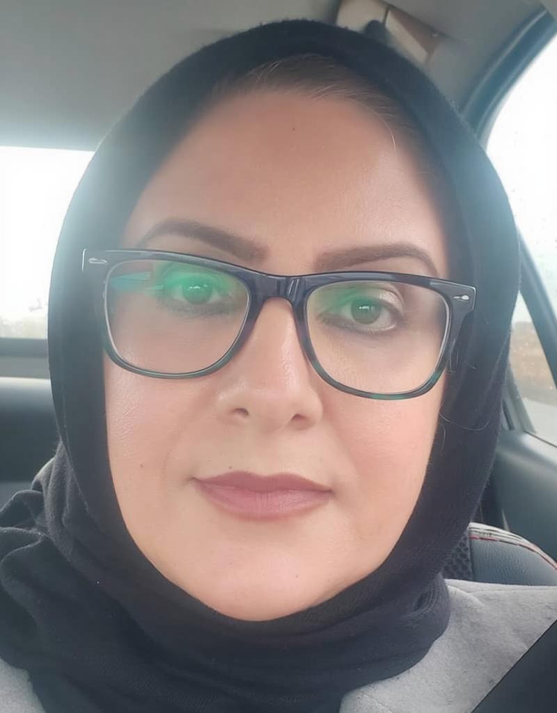 A close-up portrait of a woman wearing glasses and a stylish black hijab, seated in a car
