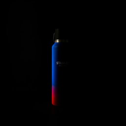 A dark room featuring a Stanley thermos that is predominantly blue and red in color, illuminated by a soft white light that highlights its surface