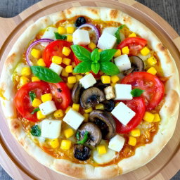 A freshly crafted pizza topped with a vibrant medley of ingredients, including succulent slices of red onions, ripe and juicy tomatoes, sweet golden corn, tender and earthy mushrooms, and creamy paneer cubes, all blanketed under a gooey layer of melted mozzarella cheese