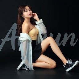 A beautiful Korean woman wearing a strapless top layered with a sheer white jacket, a short black skirt, and sneakers, sitting on the floor sideways while glancing forward gracefully