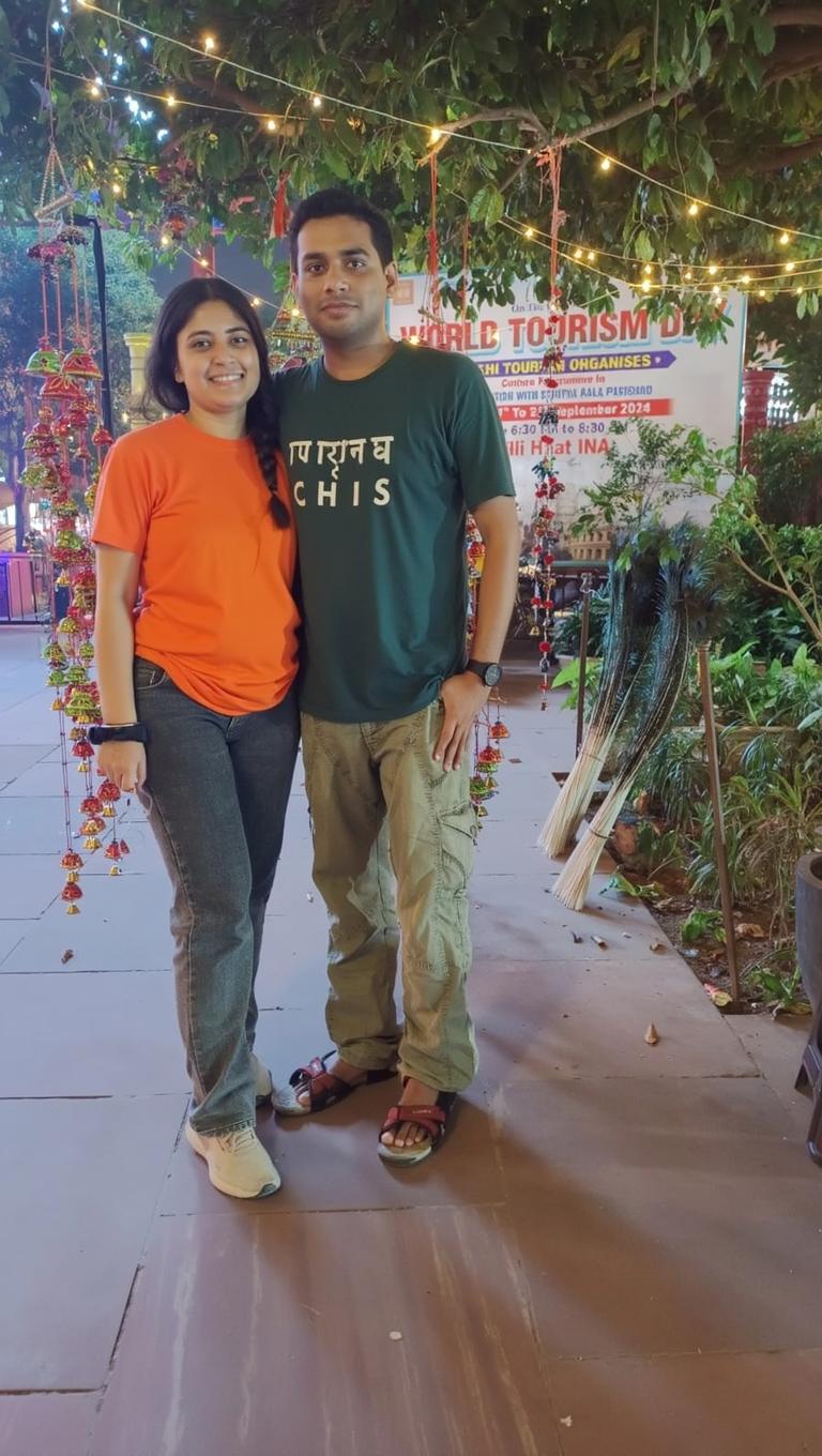 A cheerful couple standing outdoors at a festive event, surrounded by colorful decorations and fairy lights