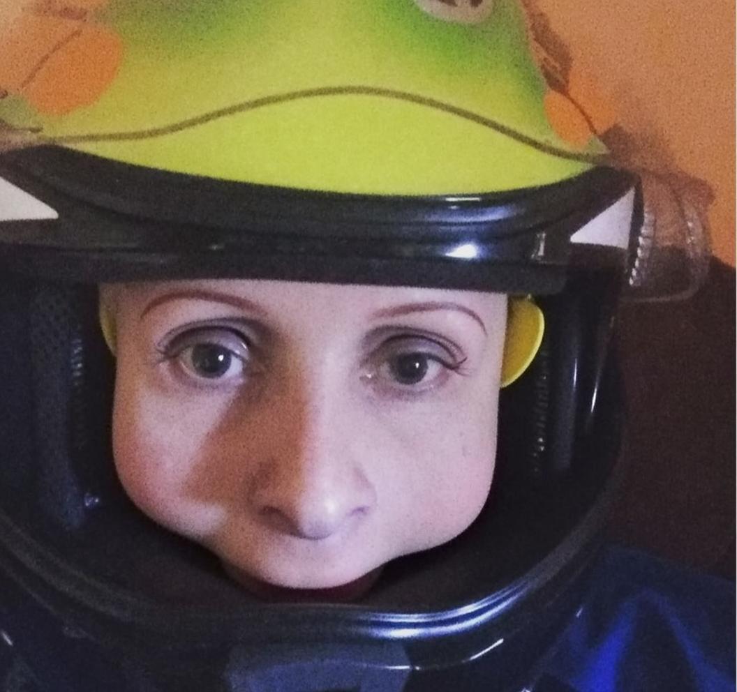 A close-up portrait of a person wearing a brightly colored motorcycle helmet designed to look like a cartoonish frog